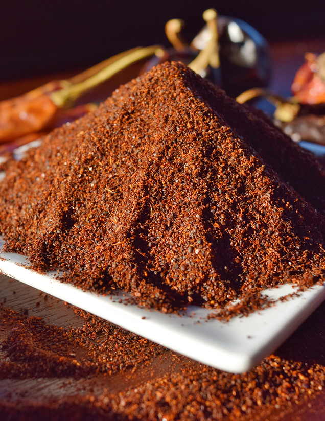 A conical mound of coarse, dark red chili powder on a white square plate